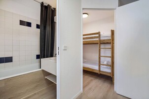 A small, compact room with a wooden bunk bed, a white sink, and a shower area with a curtain.
