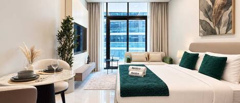 Une chambre d’hôtel moderne équipée d’un lit, d’un coin salon avec une table et d’une grande fenêtre donnant sur un paysage agréable.