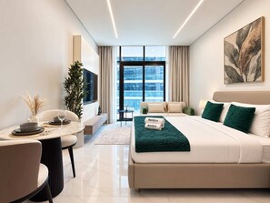 A modern hotel room with a bed, a seating area with a table, and a large window offering a view. - Rentico | Resort Studio | Pool, Sauna, Gym, BBQ (Dubai)