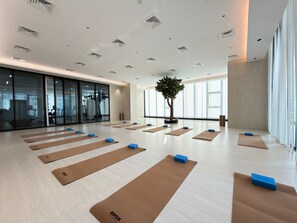 A spacious room with multiple yoga mats arranged for exercise, a large window providing natural light, and a potted tree adding greenery. - Rentico | Resort Studio | Pool, Sauna, Gym, BBQ (Dubai)
