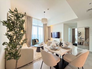 Ein moderner Essbereich mit Tisch für vier Personen, einer Couch, einem Fernseher und einem großen Fenster mit Vorhängen.