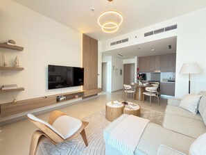 A modern living room with a flat-screen TV, wooden furniture, and a dining area with a round table. - Rentico | Luxury 1BR Hills Park | Pool & Mall (Dubai)