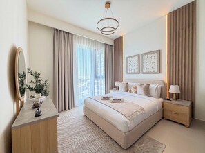 A modern bedroom with a large bed, a bedside table, a nightstand, a mirror, and a view of the city. - Rentico | Luxury 1BR Hills Park | Pool & Mall (Dubai)