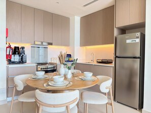 A modern kitchen with wooden cabinets, a stainless steel refrigerator, and a dining table set with white plates and bowls. - Rentico | Luxury 1BR Hills Park | Pool & Mall (Dubai)