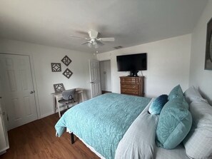 Une chambre à coucher comprenant un lit, un bureau, une chaise, un téléviseur et un ventilateur de plafond.