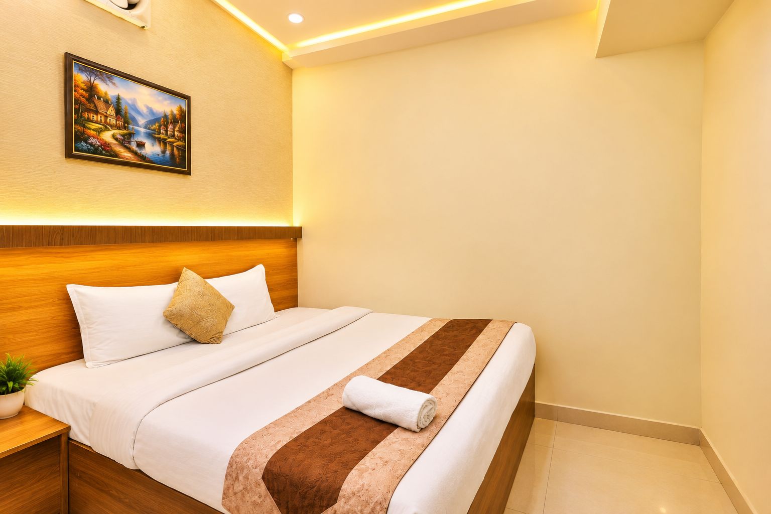 A hotel room with a neatly made bed, a painting on the wall, and a small plant on the nightstand.