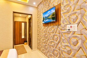 A hotel room with a wooden door, a television mounted on a geometric-patterned wall, and a power outlet.