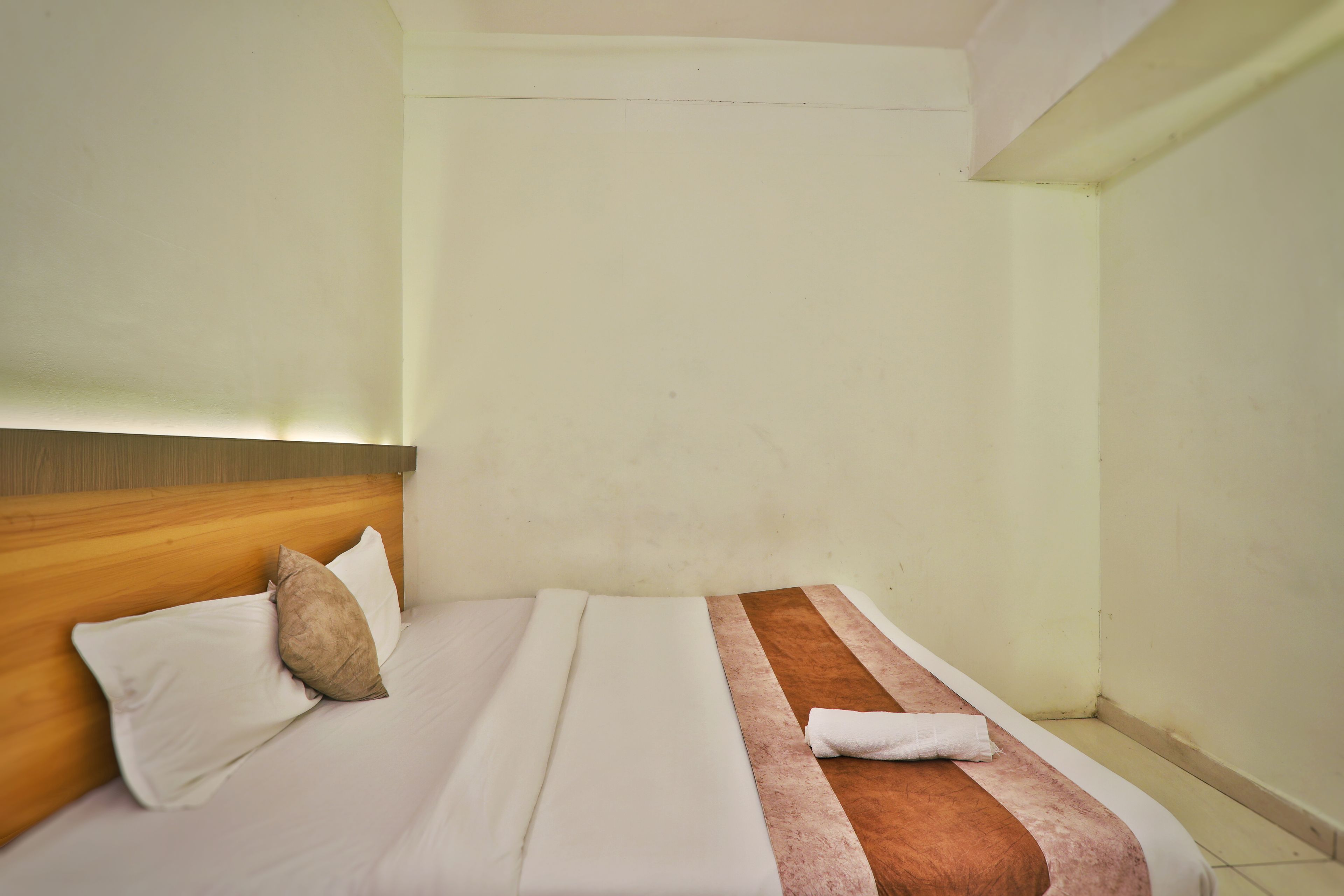 Habitación de hotel con cama, almohadas, cabecera de madera y toalla.