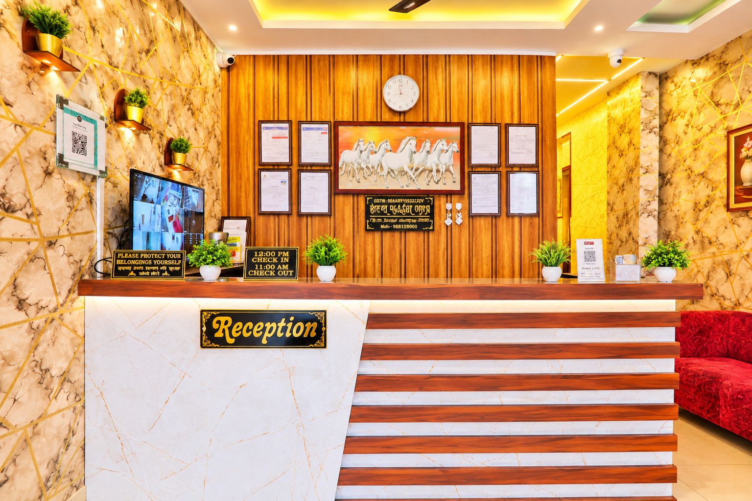 A hotel reception area with a marble wall, wooden paneling, a clock, framed certificates, and a reception desk with a sign.