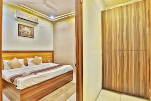 A bedroom with a wooden bed, a ceiling fan, an air conditioning unit, and a wardrobe. - Hotel Kasol Inn (Gorakhpur)