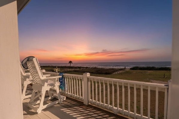 A balcony with a view of the ocean at sunset, white railings, and a single lounge chair. - Amazing Views, 4bd/2bth, Deck, Easy Walk to Beach (Bolivar Peninsula)