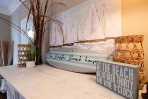 Ein Strandambiente mit einem Schild, auf dem 'The Benitez Beach house' steht, und einem weiteren Schild mit der Aufschrift 'AM STRAND GIBT ES BIER, DREIZEHN UND WEIN UHR.'