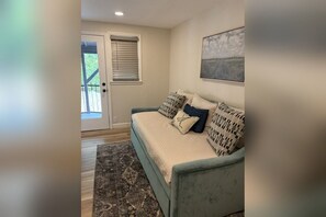 A room with a sofa, a door leading outside, and a painting on the wall. - Adorable 3-bedroom house with hidden Game Room (Granbury)