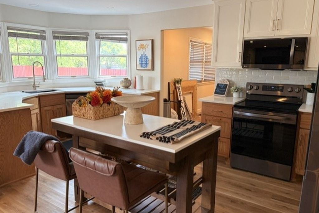 A kitchen with a central island, wooden cabinets, a stainless steel oven, and a window with blinds.