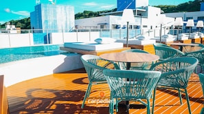 Un área junto a la piscina con un deck de madera, sillas de mimbre verde y una pequeña mesa redonda.