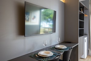 A modern dining area with a flat-screen TV mounted on the wall, a table set for two with plates and glasses, and a refrigerator to the right. - Setai Yacht - Flat in Cabo Branco by Carpediem (João Pessoa)
