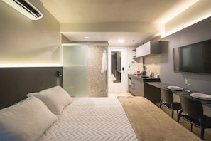 Una habitación de hotel con una cama, un escritorio, un televisor y una kitchenette.