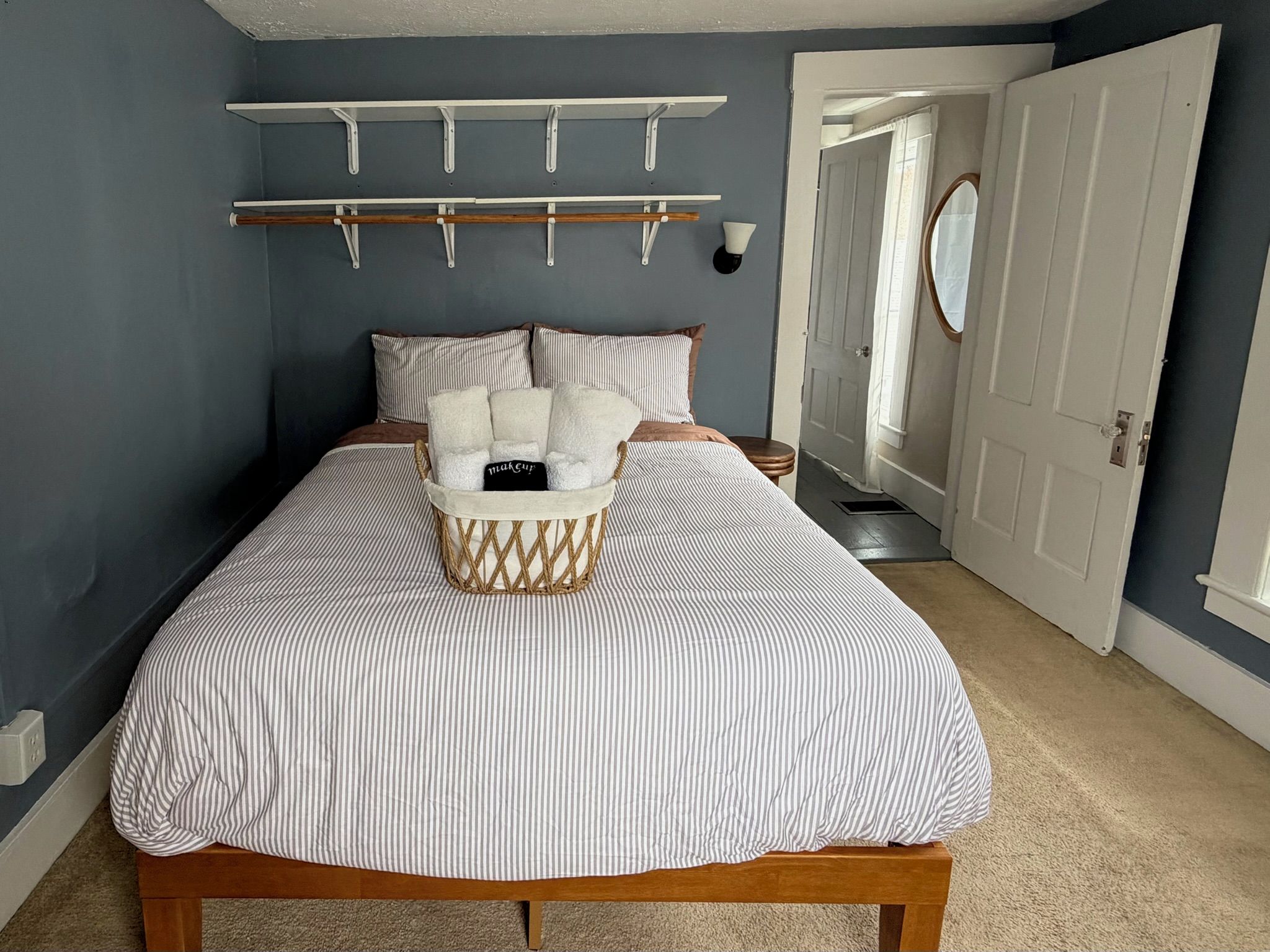 A bedroom with a bed, a basket of towels, a coat rack, and a door.
