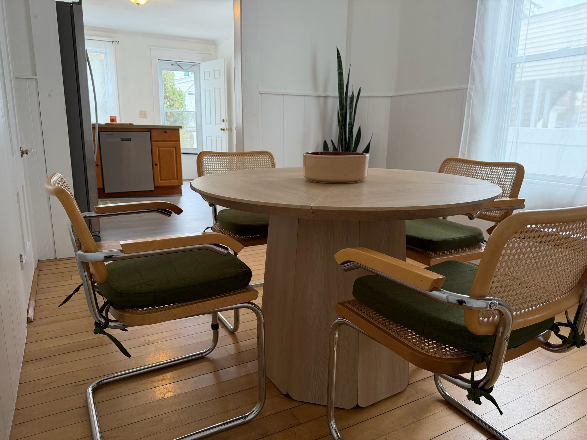 En matplats med ett runt bord, fyra stolar med gröna kuddar och en krukväxt på bordet.