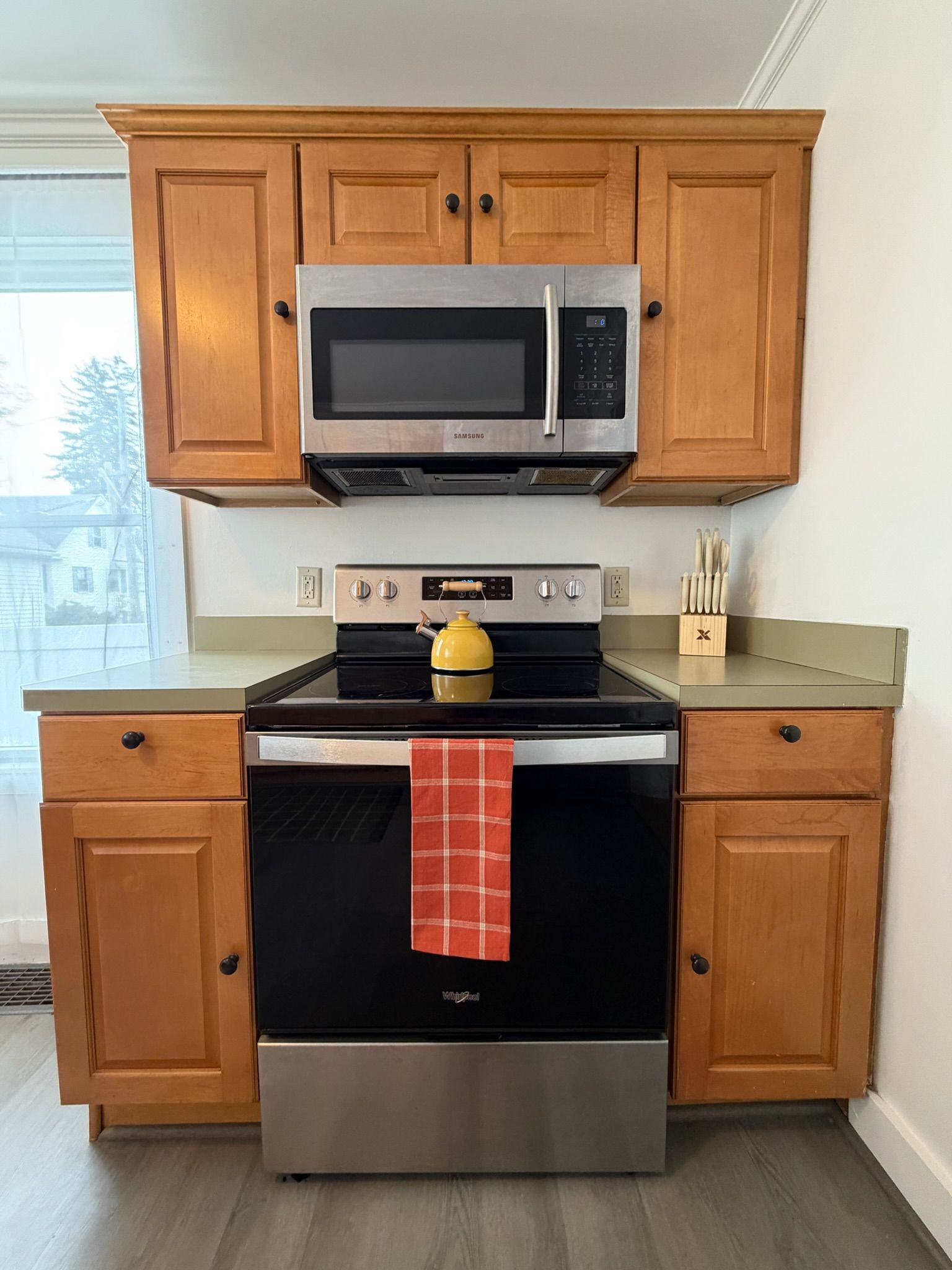 A kitchen with wooden cabinets, a stainless steel microwave, an oven, and a kettle on the stove.