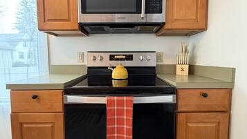 A kitchen with wooden cabinets, a stainless steel microwave, an oven, and a kettle on the stove.