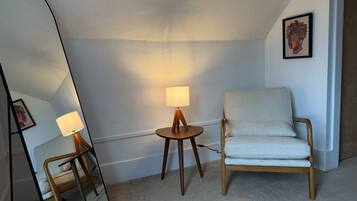 Ett rum med en stol, ett litet bord med en lampa och en spegel.