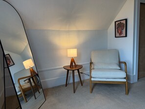 Ett rum med en stol, ett litet bord med en lampa och en spegel.