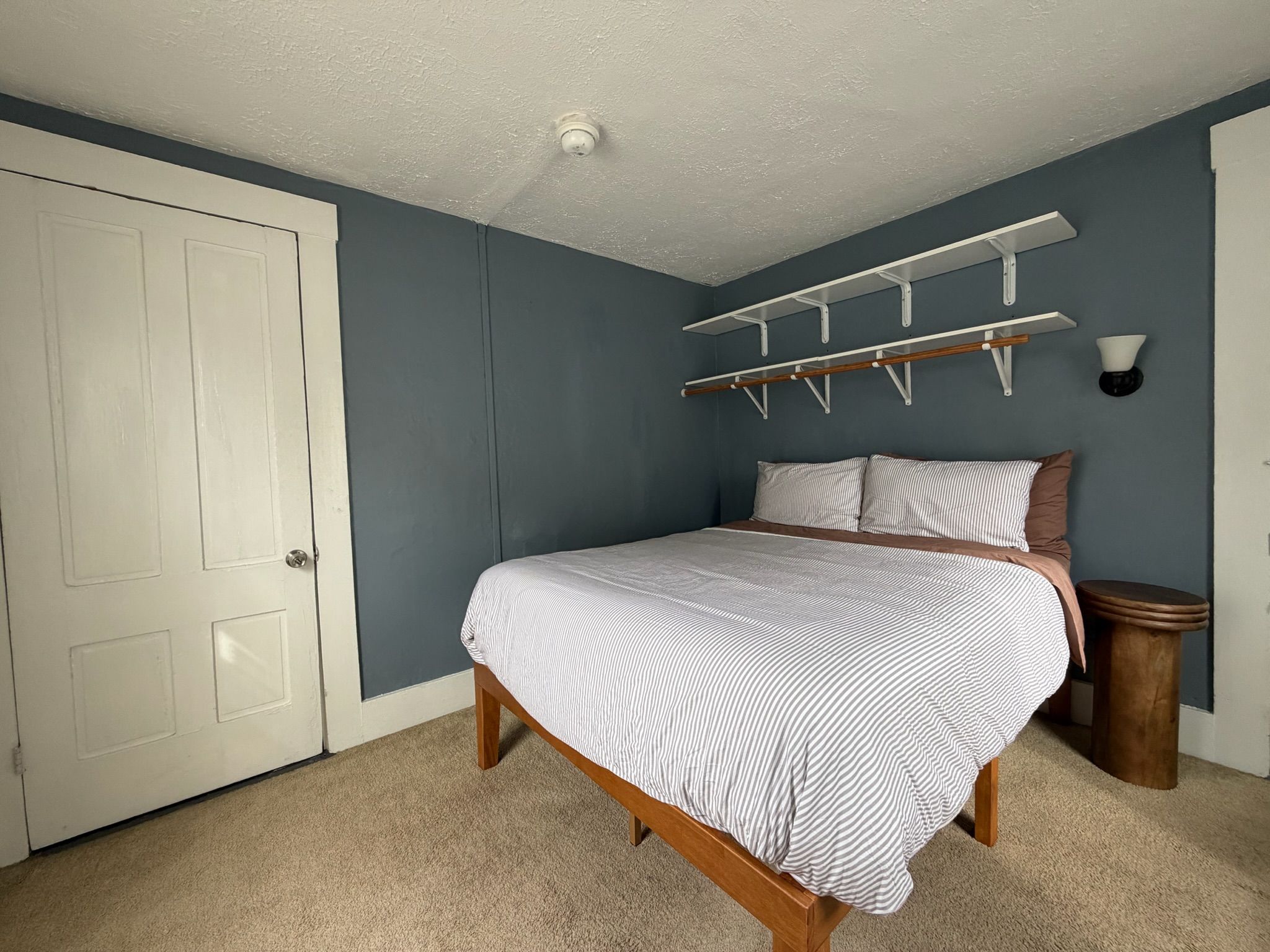 Een slaapkamer met een bed, een kledingkast, een wandplank en een nachtkastje.