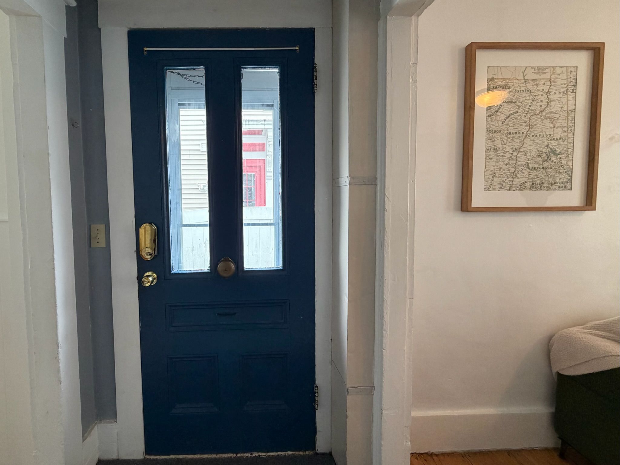 A dark blue door with two glass panels and a brass handle, a framed map on the wall, and a partial view of a room with a light-colored floor.