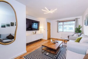 A modern living room with a flat-screen TV, a sofa, a coffee table, and a large mirror. - 3 Bed 2 Bath house near City Centre, Universities & MRI (Greater Manchester)