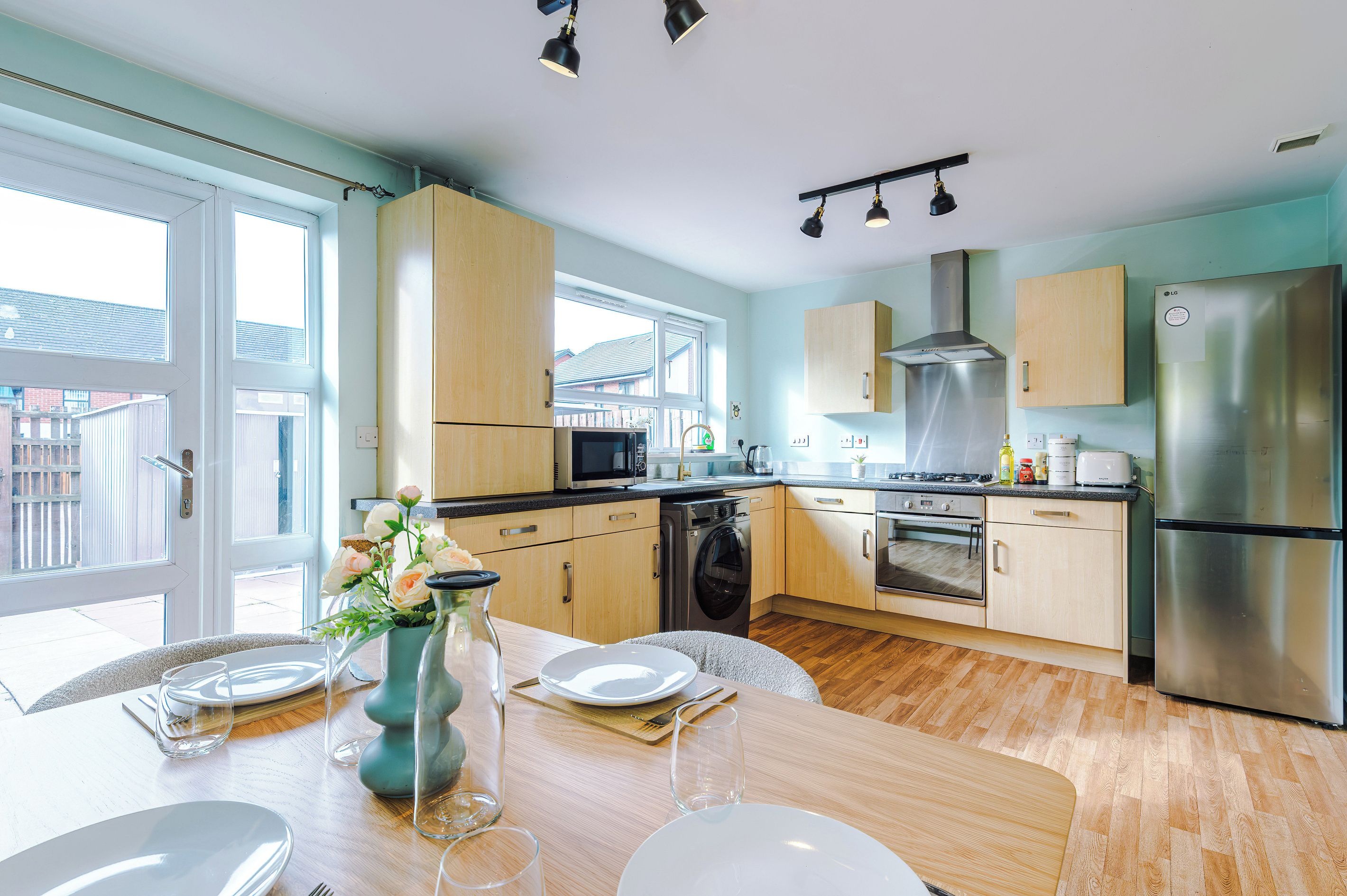 Una cocina moderna con armarios de madera, electrodomésticos de acero inoxidable y una zona de comedor preparada para cuatro.