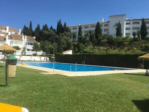A swimming pool surrounded by well-maintained grass, with buildings in the background. - House Sleeps 6 - Communal Pool - Patio & Bbq (Mijas)