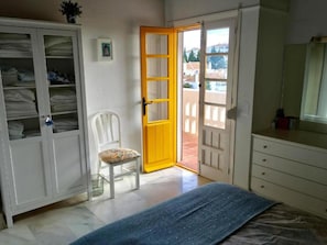 A bedroom with a bed, a chair, a wardrobe, and a door leading to an outdoor area. - House Sleeps 6 - Communal Pool - Patio & Bbq (Mijas)