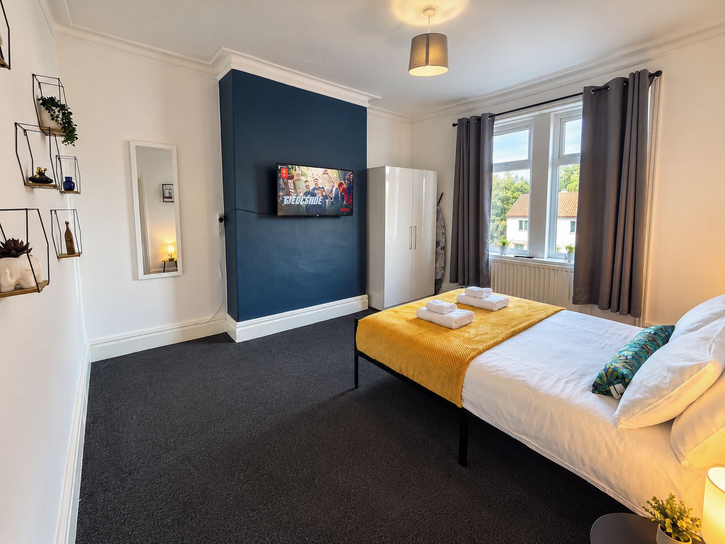 Ein Hotelzimmer mit Bett, Flachbildfernseher, Kleiderschrank und einem fenster mit Vorhängen.