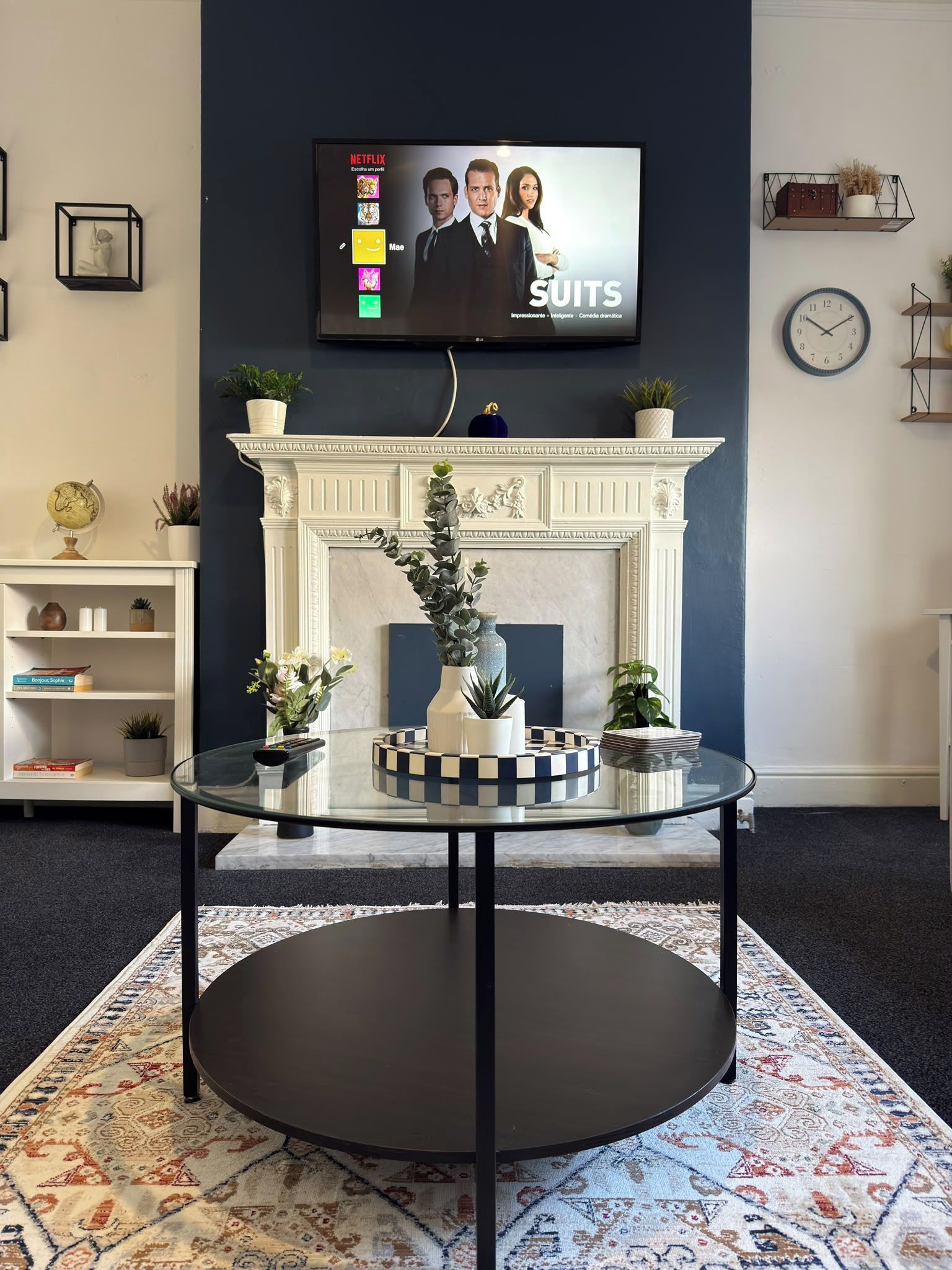A living room with a fireplace, a glass coffee table, and a flat-screen TV displaying a Netflix interface.