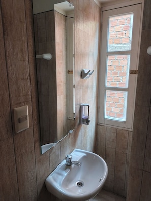 Een badkamer met een witte wastafel, een spiegel, een handdoekhouder en een raam met baksteenmotief.