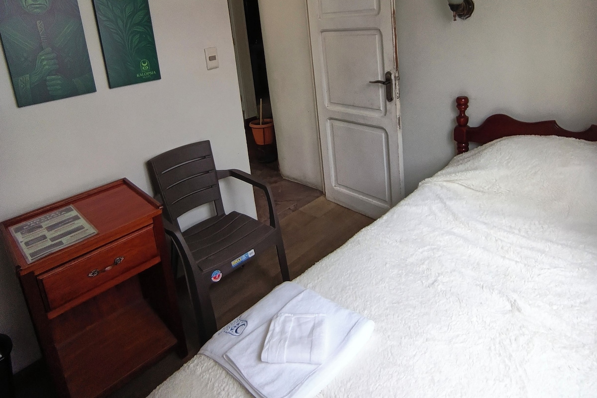 Een hotelkamer met een bed, een bureau met stoel, en twee kunstwerken aan de muur.