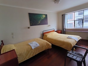 Een kamer met twee bedden, een houten bureau, een stoel, een schilderij aan de muur en een raam met uitzicht op gebouwen.