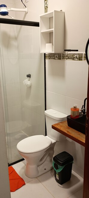 Ein Badezimmer mit Toilette, Duschkabine, Waschbecken und Seifenspender sowie einem Mülleimer.