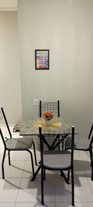 A dining area with a glass-top table, black metal chairs, and a framed artwork on the wall.