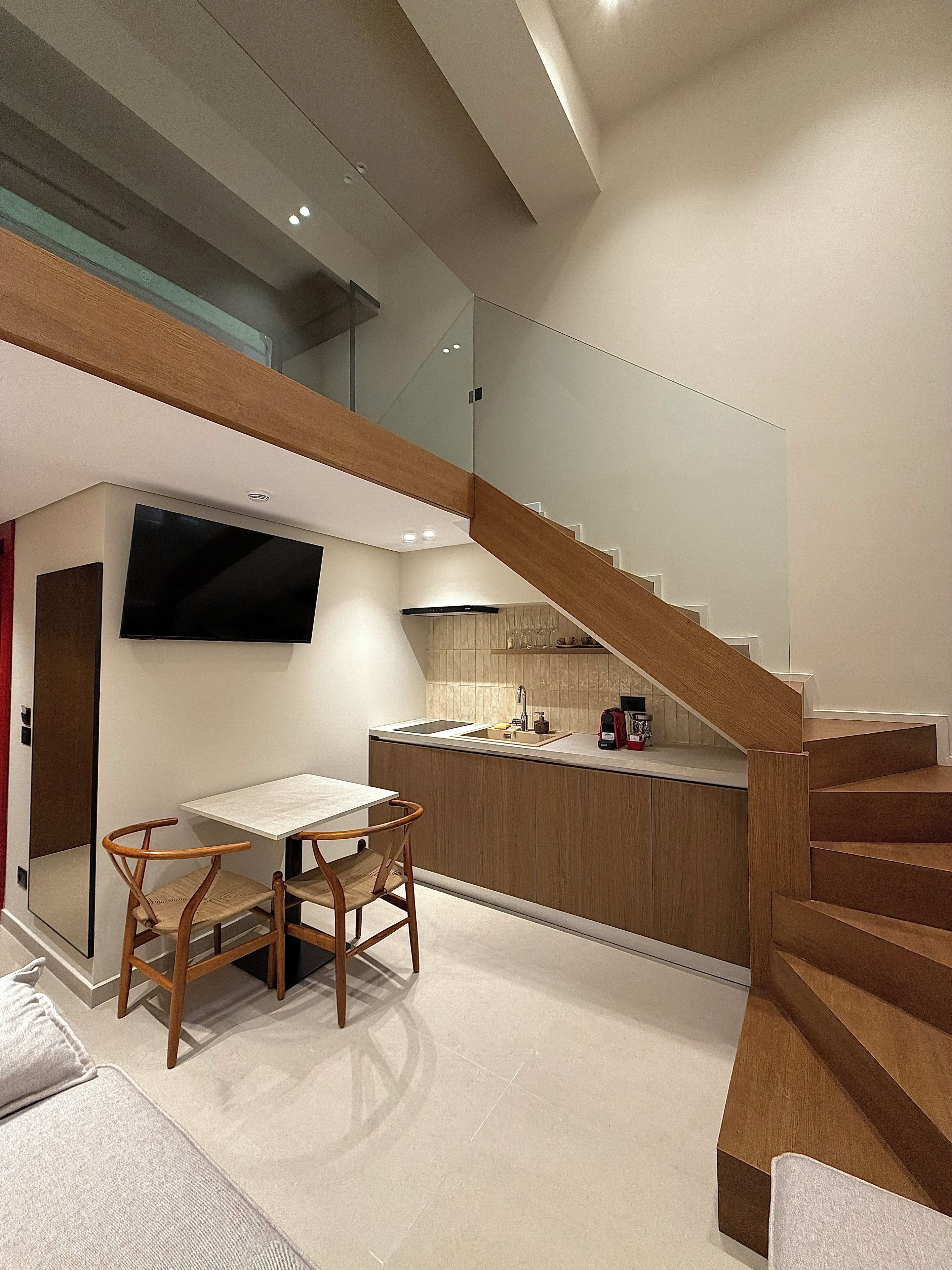 A modern kitchen with a wooden staircase, a dining area with a table and chairs, and a flat-screen TV mounted on the wall.