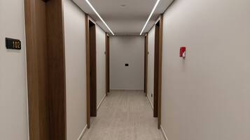 Un pasillo con puertas de madera, un detector de incendios y un cartel con un número.