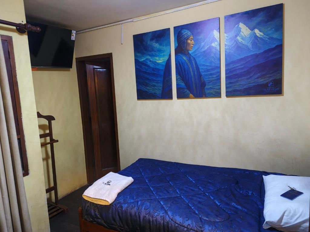 Una habitación con una cama, un televisor montado en la pared y tres cuadros.