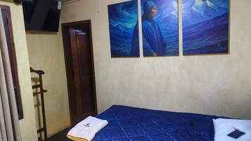 Una habitación con una cama, un televisor montado en la pared y tres cuadros.