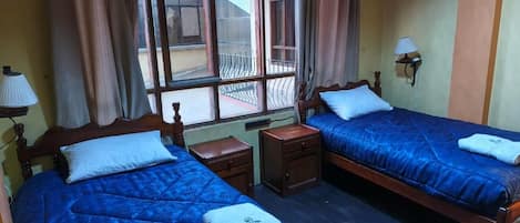 Habitación de hotel con dos camas, una ventana, una mesita de noche y una lámpara.