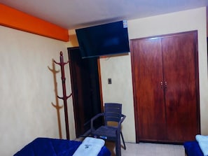 Una habitació amb llit, cadira, armari i televisió.