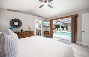 A bedroom with a large bed, a dresser, a chair, and a view of a pool through a glass door. - Naples Duo 1 | 2 Homes • Pools • King Beds (Naples)