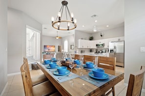 A modern kitchen with stainless steel appliances, a dining area with blue tableware, and a chandelier. - Naples Duo 1 | 2 Homes • Pools • King Beds (Naples)