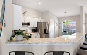 A modern kitchen with white cabinets, stainless steel appliances, a marble countertop, and a small potted plant. - Naples Duo 1 | 2 Homes • Pools • King Beds (Naples)