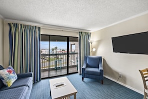 Ein Hotelzimmer mit Balkon, einer Couch, einem Sessel, einem Couchtisch und einem Flachbildfernseher.